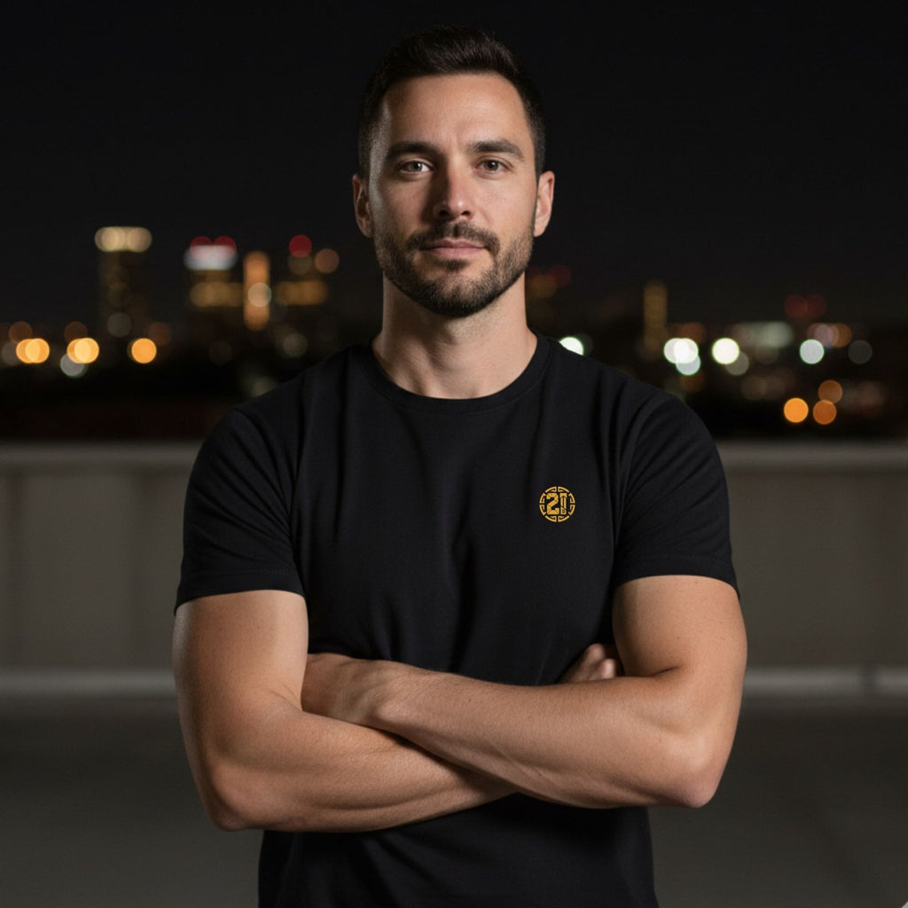 Man wearing a black t-shirt with a logo, standing against a cityscape at night.